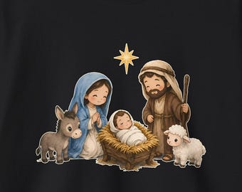 Op de afbeelding: Een zwart shirt met lange mouwen voorzien van een kleurrijke afbeelding van een kerststal. De illustratie toont een persoon met een blauwe hoofddoek, een persoon in bruine gewaden met een staf, een baby in een kribbe, een ezel, een schaap en een ster.