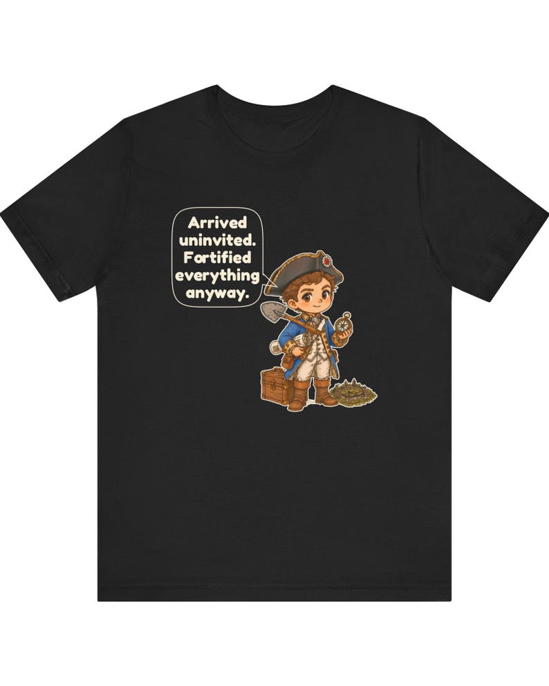 May include: A black t-shirt featuring a cartoon illustration of a historical explorer in a blue coat and tricorn hat, holding a shovel and compass next to a wooden chest. A speech bubble contains the text: Arrived uninvited. Fortified everything anyway.