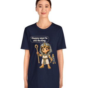 Może przedstawiać: Granatowy t-shirt z grafiką przedstawiającą faraona z kresk&oacute;wki trzymającego laskę i bicz. Nad postacią znajduje się dymek z tekstem: Mummy says I'm still the king. Faraon ma na głowie niebiesko-złote nakrycie głowy w paski.