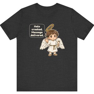 May include: A dark gray t-shirt featuring a cartoon angel with brown hair, white wings, and a gold halo. The angel holds a scroll and waves. A speech bubble contains the text: Halo crooked. Message delivered.