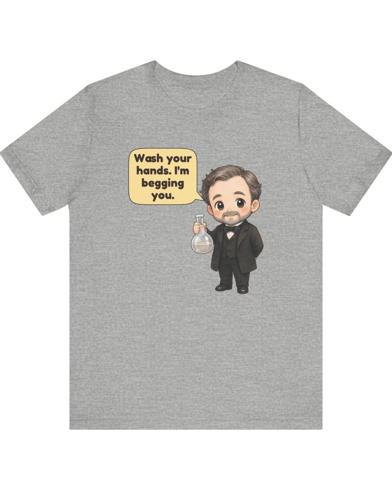 May include: A heather gray t-shirt featuring a cartoon illustration of a man in a black suit and bowtie holding a glass flask. A speech bubble next to him contains the text: Wash your hands. I'm begging you.
