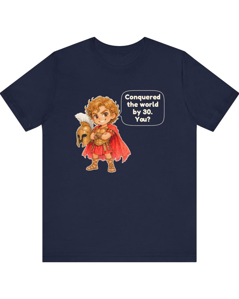 May include: A navy blue short-sleeve t-shirt featuring a cartoon illustration of a warrior in golden armor and a red cape holding a helmet. A speech bubble next to the character contains the text: Conquered the world by 30. You?