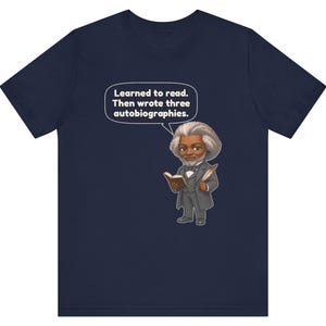 Puede incluir: Una camiseta azul marino con una ilustraci&oacute;n de estilo caricatura de Frederick Douglass sosteniendo un libro y una pluma. Un globo de texto sobre &eacute;l contiene el texto: Learned to read. Then wrote three autobiographies. El dise&ntilde;o est&aacute; centrado.