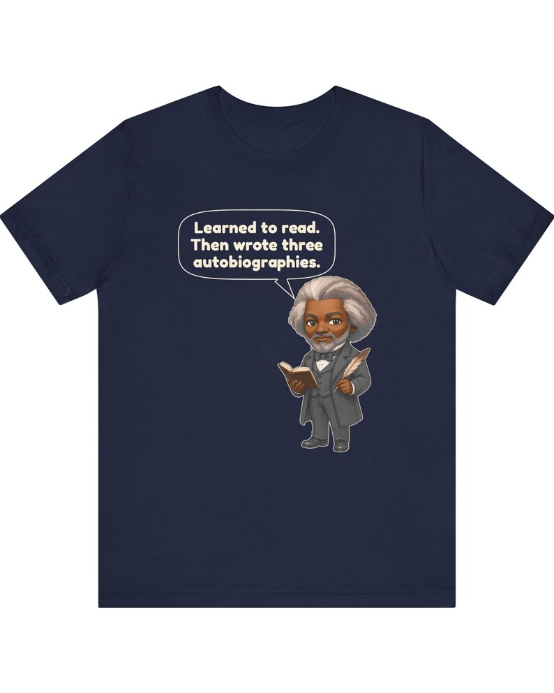 Puede incluir: Una camiseta azul marino con una ilustraci&oacute;n de estilo caricatura de Frederick Douglass sosteniendo un libro y una pluma. Un globo de texto sobre &eacute;l contiene el texto: Learned to read. Then wrote three autobiographies. El dise&ntilde;o est&aacute; centrado.