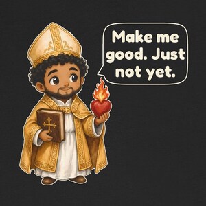 May include: A black t-shirt featuring a cartoon illustration of a bishop wearing gold vestments and a mitre. The figure holds a brown book with a cross and a flaming red heart. A speech bubble contains the text: Make me good. Just not yet.