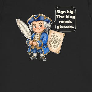 May include: A black t-shirt featuring a cartoon illustration of a person in an 18th-century blue coat, white wig, and tricorn hat. The person holds a white quill and a scroll. A speech bubble contains the text: Sign big. The king needs glasses.