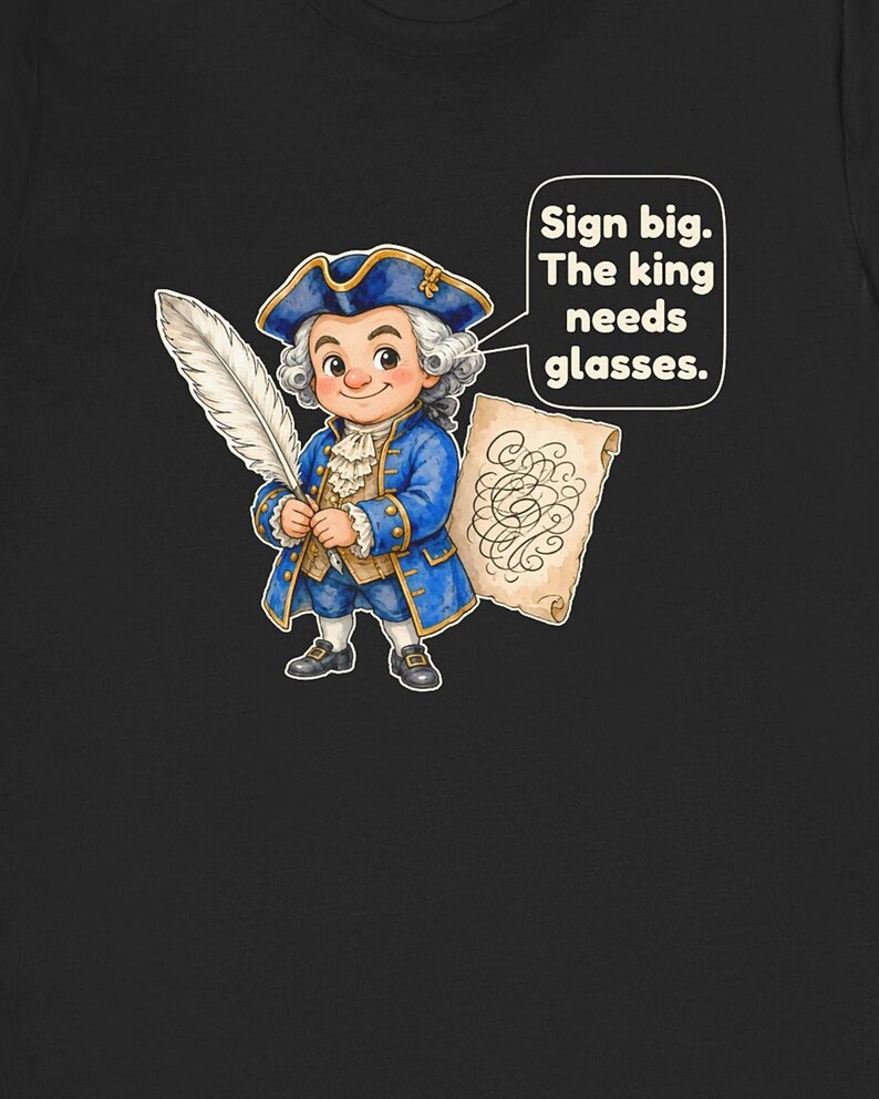 May include: A black t-shirt featuring a cartoon illustration of a person in an 18th-century blue coat, white wig, and tricorn hat. The person holds a white quill and a scroll. A speech bubble contains the text: Sign big. The king needs glasses.