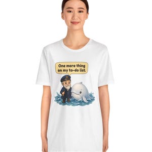 May include: A white short-sleeve t-shirt featuring a graphic of a sea captain standing next to a white whale in blue water. Above them is a yellow speech bubble containing the black text, One more thing on my to-do list.