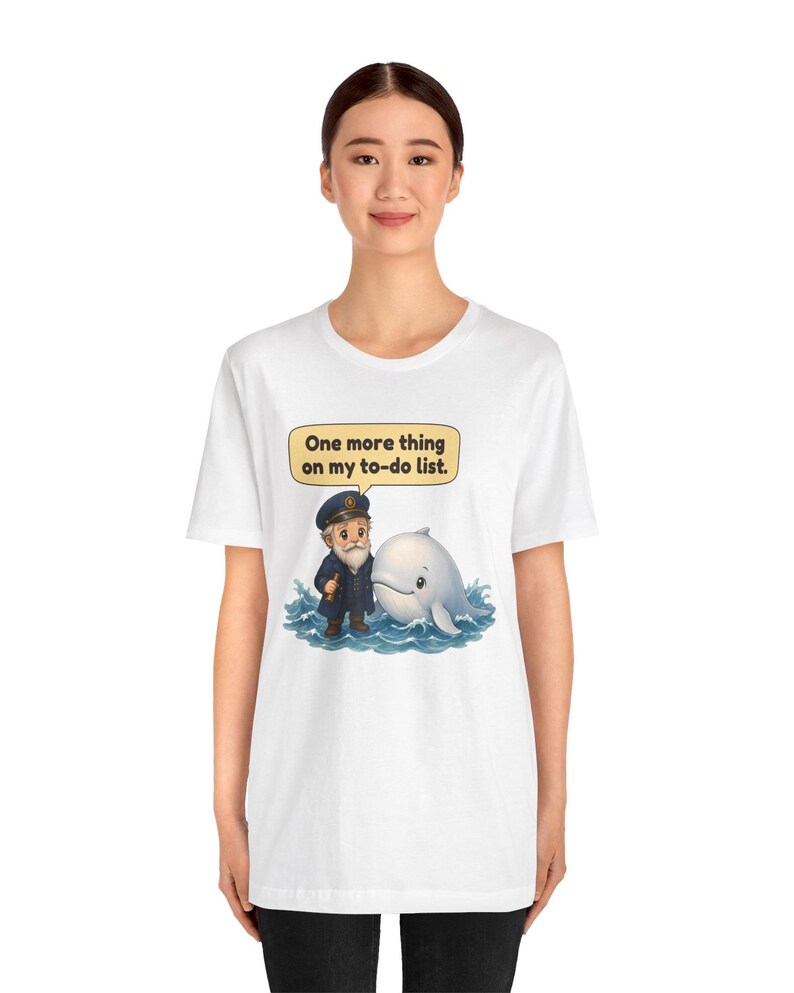 May include: A white short-sleeve t-shirt featuring a graphic of a sea captain standing next to a white whale in blue water. Above them is a yellow speech bubble containing the black text, One more thing on my to-do list.