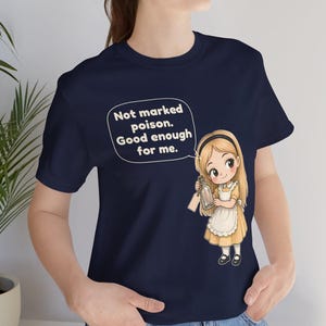 May include: A navy blue t-shirt featuring a graphic of a blonde character in a yellow dress and white apron holding a glass bottle. A speech bubble above the character contains the text: Not marked poison. Good enough for me.
