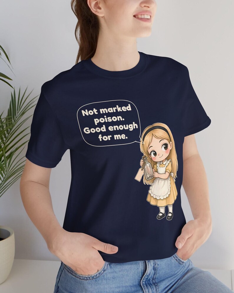 May include: A navy blue t-shirt featuring a graphic of a blonde character in a yellow dress and white apron holding a glass bottle. A speech bubble above the character contains the text: Not marked poison. Good enough for me.