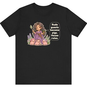 May include: A black t-shirt featuring a graphic of a character in a purple dress holding a wand and a cup, surrounded by three small pigs. A speech bubble next to the character contains the text: Rude guests become pigs. House rules.
