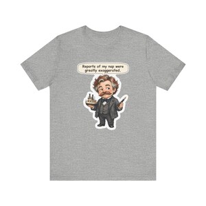 Watercolor chibi Mississippi riverboat author with a bushy moustache, navy bow tie and charcoal suit, holding a model riverboat and a fountain pen, with the speech bubble "Reports of my nap were greatly exaggerated." printed on a tee