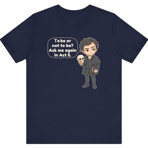 以下が含まれることがあります： 頭蓋骨を持ったキャラクターの漫画風イラストが描かれたネイビーブルーの半袖Tシャツ。吹き出しには「To be or not to be? Ask me again in Act 5.」というテキストがあります。キャラクターは暗い色のコートを着て本を持っています。