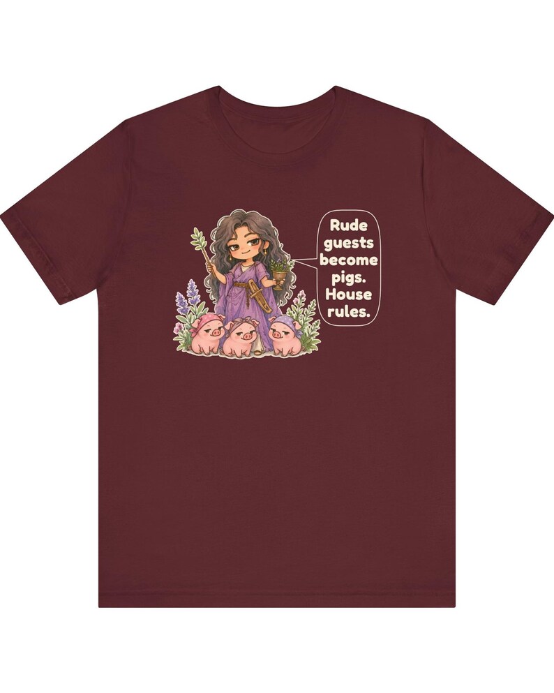 May include: A maroon short-sleeved t-shirt featuring a graphic of a character in a purple dress holding a staff and cup, surrounded by three small pigs. The text reads: Rude guests become pigs. House rules.