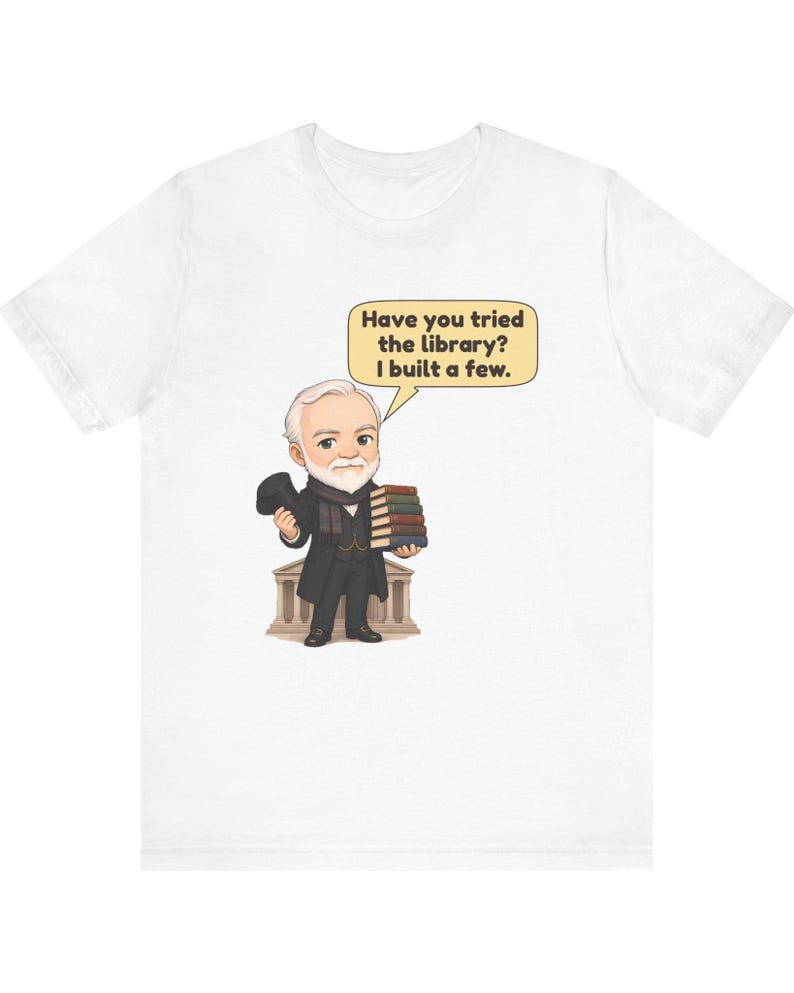 May include: A white t-shirt featuring a cartoon illustration of an older man with a white beard, wearing a black coat and holding a stack of books. A speech bubble above him contains the text: Have you tried the library? I built a few.
