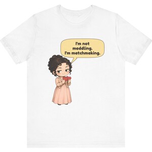 K&ouml;nnte beinhalten: Ein wei&szlig;es T-Shirt mit einer Cartoon-Illustration einer Person mit dunklem, lockigem Haar, die ein hellrosa Kleid und eine Jacke tr&auml;gt und zwei rote Herzen h&auml;lt. Eine gelbe Sprechblase dar&uuml;ber enth&auml;lt den Text: I'm not meddling. I'm matchmaking.