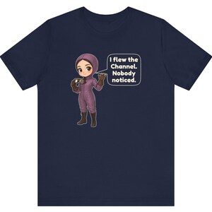 Puede incluir: Una camiseta azul marino con una ilustraci&oacute;n de dibujos animados de un personaje con traje de vuelo morado y botas marrones sosteniendo unas gafas. Un globo de texto junto al personaje contiene: I flew the Channel. Nobody noticed.