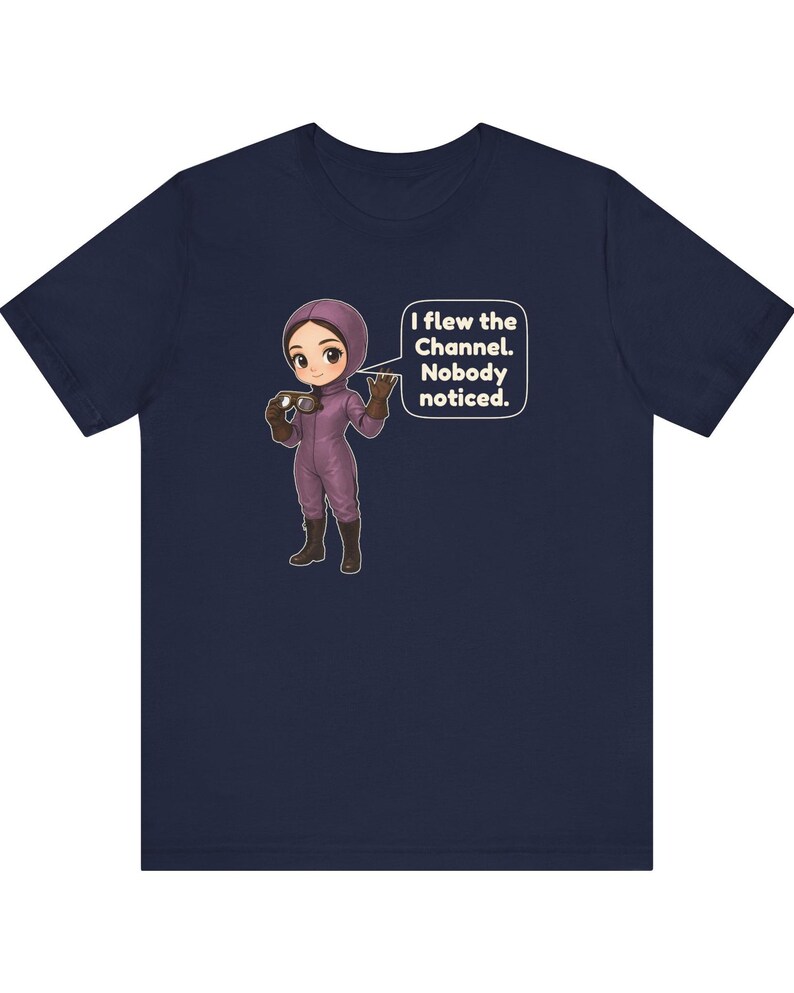 Puede incluir: Una camiseta azul marino con una ilustraci&oacute;n de dibujos animados de un personaje con traje de vuelo morado y botas marrones sosteniendo unas gafas. Un globo de texto junto al personaje contiene: I flew the Channel. Nobody noticed.