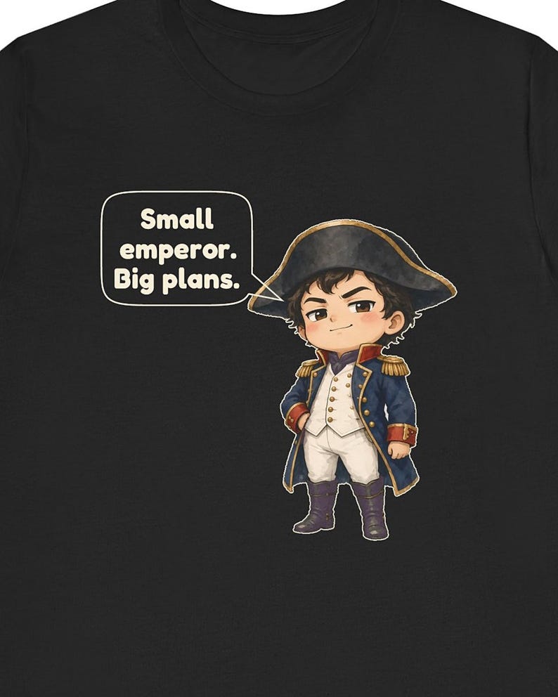 May include: A black t-shirt featuring a cartoon illustration of a small emperor in a blue military coat, white vest, and black bicorne hat. A speech bubble next to the character contains the text: Small emperor. Big plans.