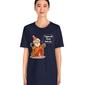 May include: A navy blue short-sleeve t-shirt featuring a graphic of a bearded figure in a red toga and party hat, holding a sickle and wheat. A speech bubble contains the text: Togas off. Party hats on. The figure has a bandaged leg.