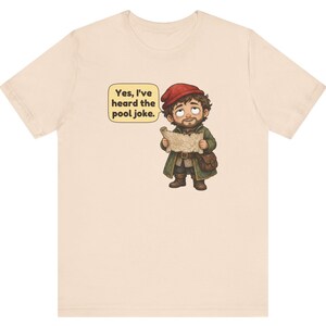 May include: A light beige t-shirt featuring a cartoon illustration of a bearded character wearing a red cap and green coat, holding a map. A speech bubble next to the character contains the text: Yes, I've heard the pool joke.
