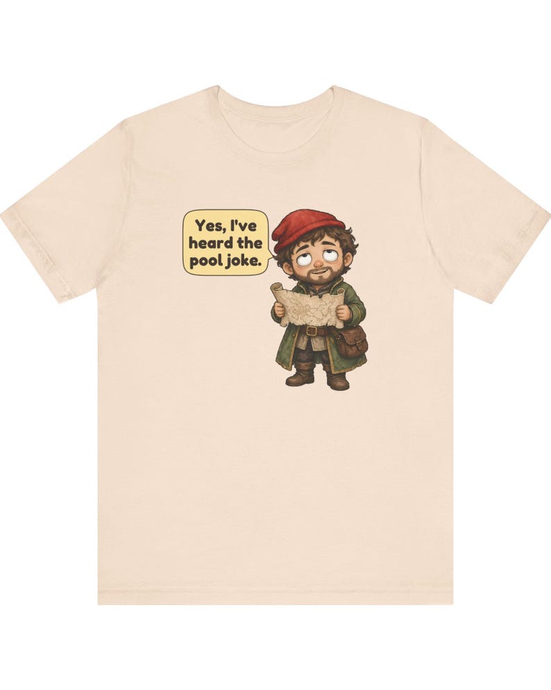 May include: A light beige t-shirt featuring a cartoon illustration of a bearded character wearing a red cap and green coat, holding a map. A speech bubble next to the character contains the text: Yes, I've heard the pool joke.