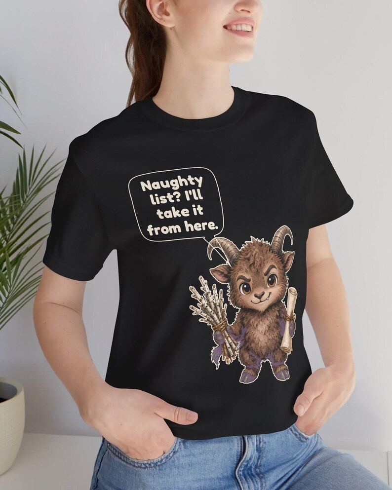 Puede incluir: Una camiseta negra con el gr&aacute;fico de una criatura marr&oacute;n con cuernos, similar a una cabra, que sostiene un manojo de ramas y un pergamino. Un globo de texto sobre la criatura contiene: Naughty list? I'll take it from here.