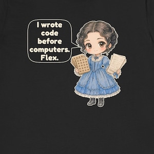 May include: A black t-shirt featuring a cartoon illustration of a person in a blue dress holding punch cards and papers. A speech bubble contains the text: I wrote code before computers. Flex. The character has dark hair and wears dark boots.