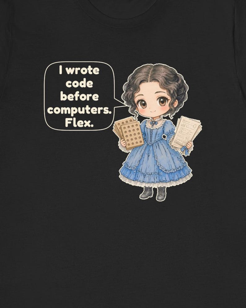 May include: A black t-shirt featuring a cartoon illustration of a person in a blue dress holding punch cards and papers. A speech bubble contains the text: I wrote code before computers. Flex. The character has dark hair and wears dark boots.
