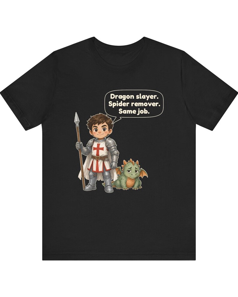 K&ouml;nnte beinhalten: Ein schwarzes T-Shirt mit einer Cartoon-Illustration eines Ritters in silberner R&uuml;stung, der einen Speer h&auml;lt und neben einem kleinen gr&uuml;nen Drachen steht. Eine Sprechblase &uuml;ber dem Ritter enth&auml;lt den Text: Dragon slayer. Spider remover. Same job.