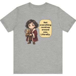 May include: A heather gray t-shirt featuring a cartoon character with dark curly hair wearing a maroon coat with fur trim, holding a golden model of a solar system. A speech bubble contains the text: Not everything revolves around you. Literally.