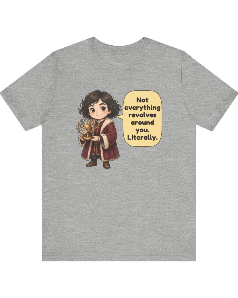 May include: A heather gray t-shirt featuring a cartoon character with dark curly hair wearing a maroon coat with fur trim, holding a golden model of a solar system. A speech bubble contains the text: Not everything revolves around you. Literally.