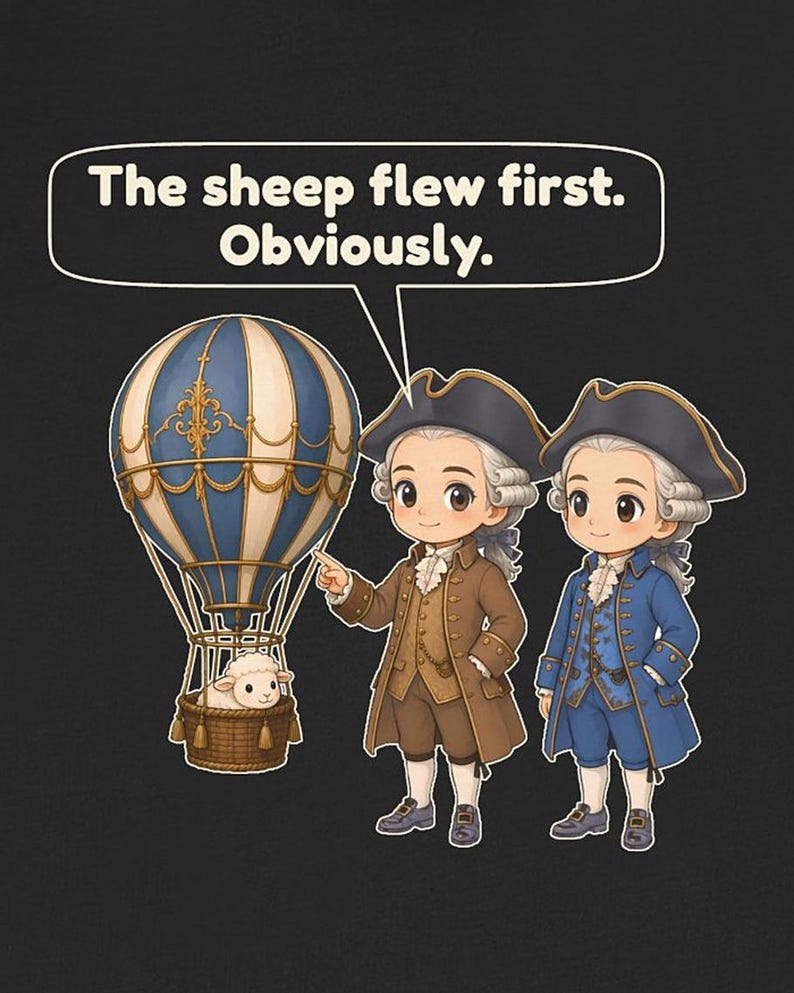 May include: A black graphic t-shirt featuring two figures in 18th-century attire standing next to a blue and white hot air balloon with a sheep in the basket. A speech bubble above them contains the text: The sheep flew first. Obviously.