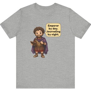 K&ouml;nnte beinhalten: Ein graumeliertes T-Shirt mit einer Cartoon-Illustration einer b&auml;rtigen Figur in r&ouml;mischer R&uuml;stung und violettem Umhang, die ein Tagebuch h&auml;lt. Eine Sprechblase enth&auml;lt den Text: Emperor by day. Journaling by night.