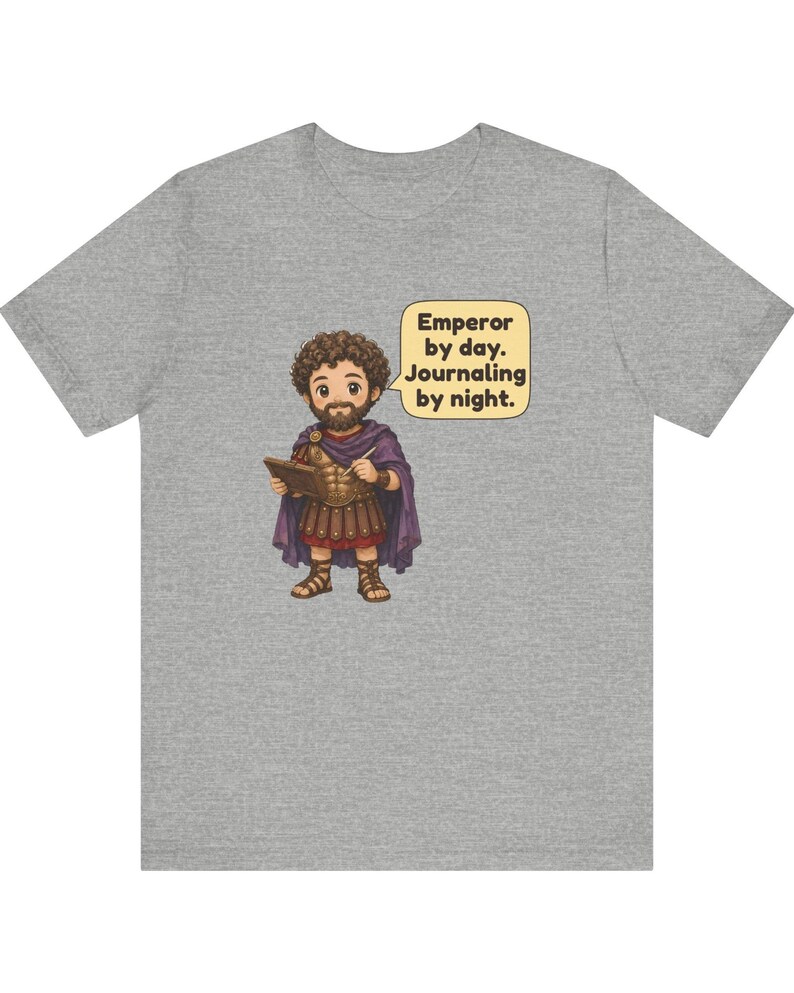 K&ouml;nnte beinhalten: Ein graumeliertes T-Shirt mit einer Cartoon-Illustration einer b&auml;rtigen Figur in r&ouml;mischer R&uuml;stung und violettem Umhang, die ein Tagebuch h&auml;lt. Eine Sprechblase enth&auml;lt den Text: Emperor by day. Journaling by night.