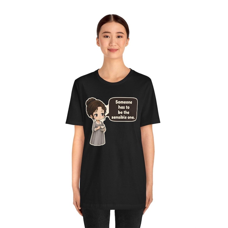 May include: A black t-shirt featuring a cartoon illustration of a person in a gray dress holding a teacup. Next to the character is a speech bubble containing the text: Someone has to be the sensible one. The design is centered on the chest.