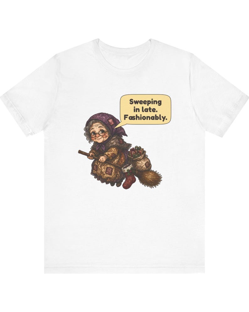 Puede incluir: Una camiseta blanca con un gr&aacute;fico de una persona mayor con un pa&ntilde;uelo morado y ropa marr&oacute;n, montada en una escoba. Un bocadillo contiene el texto: Sweeping in late. Fashionably. La persona lleva un saco consigo.