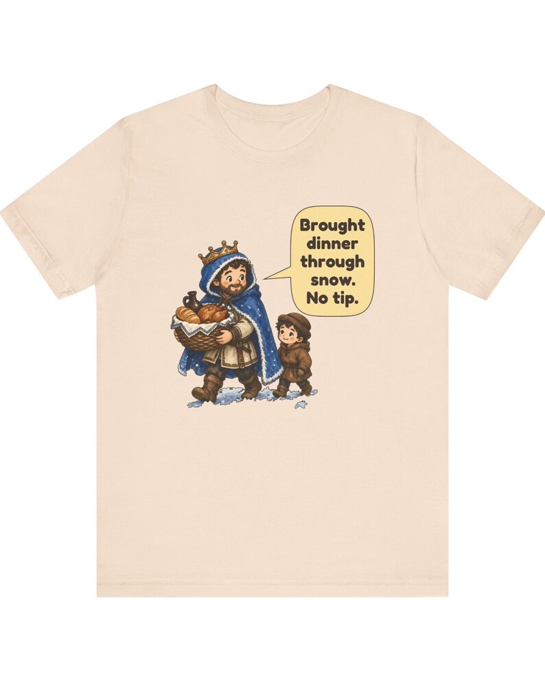 May include: A light beige t-shirt featuring a cartoon illustration of a king in a blue cloak carrying a basket of food with a child. A speech bubble contains the text: Brought dinner through snow. No tip. The design is centered on the chest.