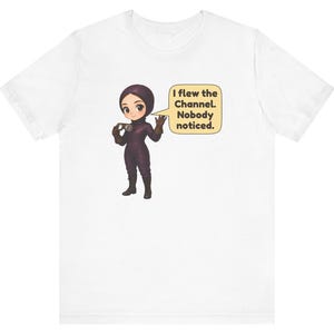 Puede incluir: Una camiseta blanca con un personaje de dibujos animados vestido con un traje de vuelo y casco de color morado oscuro, sosteniendo unas gafas. Un bocadillo amarillo junto al personaje contiene el texto: I flew the Channel. Nobody noticed.