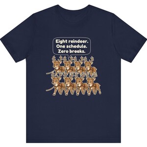 K&ouml;nnte beinhalten: Ein kurz&auml;rmeliges T-Shirt in Marineblau mit einer Grafik von acht braunen Rentieren in zwei Reihen. &Uuml;ber den Rentieren befindet sich eine wei&szlig;e Sprechblase mit dem Text: Eight reindeer. One schedule. Zero breaks.