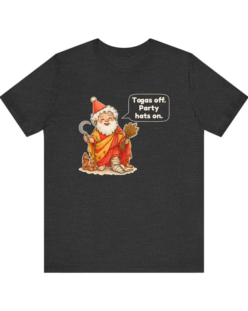 May include: A dark heather gray t-shirt featuring a cartoon illustration of a bearded figure in a red and yellow robe wearing a party hat, holding a sickle and wheat, with a speech bubble that reads, "Togas off. Party hats on."