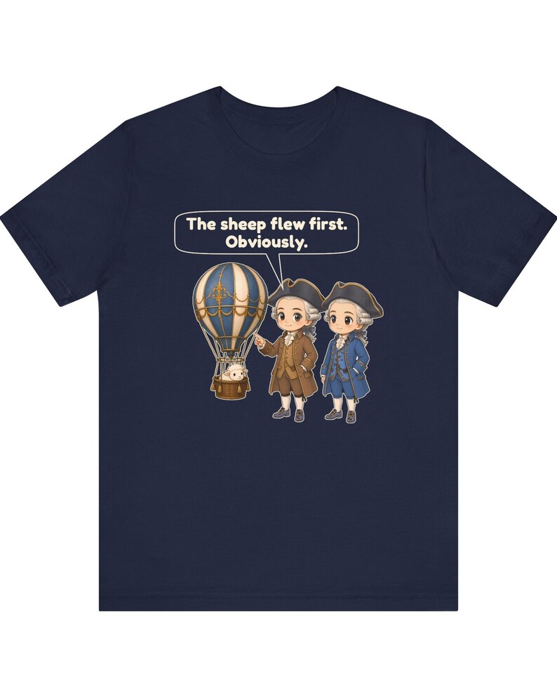May include: A navy blue t-shirt featuring a graphic of two figures in 18th-century attire standing next to a hot air balloon with a sheep in the basket. A speech bubble above them contains the text: The sheep flew first. Obviously.