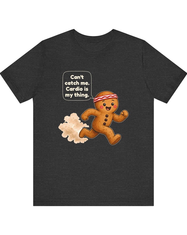 May include: A dark charcoal grey t-shirt featuring a graphic of a running gingerbread person wearing a red and white headband. A speech bubble above the character contains the text: Can't catch me. Cardio is my thing. A dust cloud follows.