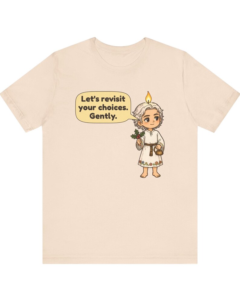May include: A light beige t-shirt featuring a graphic of a cartoon character with a candle flame on their head, holding a sprig of holly and a small kettle. A speech bubble contains the text: Let's revisit your choices. Gently.