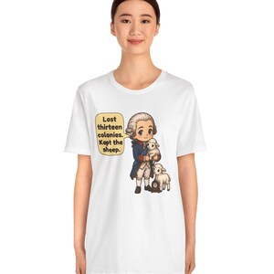 Peut inclure: Un t-shirt blanc avec une illustration de style dessin anim&eacute; repr&eacute;sentant un personnage historique en manteau bleu tenant un petit mouton blanc, avec un autre mouton &agrave; c&ocirc;t&eacute;. Une bulle contient le texte : Lost thirteen colonies. Kept the sheep.