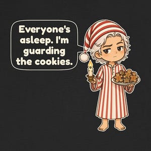 Op de afbeelding: Een zwart t-shirt met een stripfiguur in een rood-wit gestreepte pyjama en een bijpassende slaapmuts. Het figuur houdt een brandende kaars en een bord met peperkoekkoekjes vast. Een tekstballon bevat de tekst: Everyone's asleep. I'm guarding the cookies.