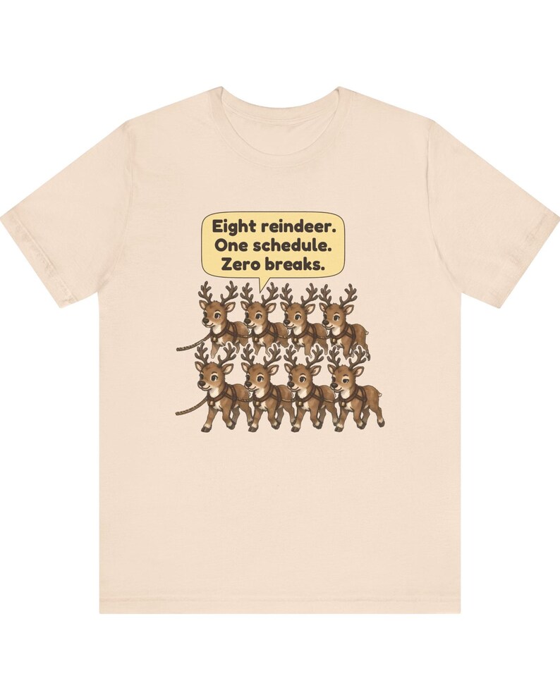 K&ouml;nnte beinhalten: Ein hellbeiges T-Shirt mit einer Grafik von acht braunen Rentieren in zwei Reihen, die durch Geschirre verbunden sind. &Uuml;ber den Rentieren befindet sich eine gelbe Sprechblase mit dem schwarzen Text: Eight reindeer. One schedule. Zero breaks.