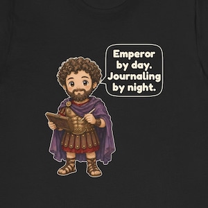 K&ouml;nnte beinhalten: Ein schwarzes T-Shirt mit einer Cartoon-Illustration einer b&auml;rtigen Person in r&ouml;mischer R&uuml;stung und einem violetten Umhang, die ein Tagebuch und einen Stift h&auml;lt. Eine Sprechblase enth&auml;lt den Text: Emperor by day. Journaling by night.