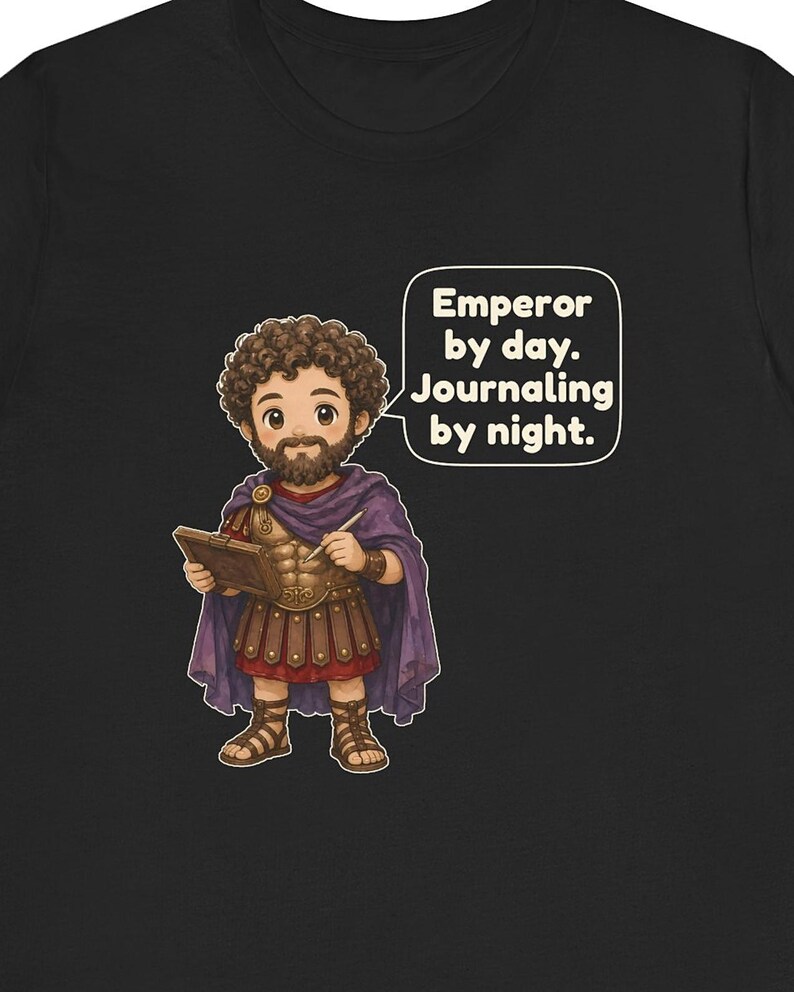 K&ouml;nnte beinhalten: Ein schwarzes T-Shirt mit einer Cartoon-Illustration einer b&auml;rtigen Person in r&ouml;mischer R&uuml;stung und einem violetten Umhang, die ein Tagebuch und einen Stift h&auml;lt. Eine Sprechblase enth&auml;lt den Text: Emperor by day. Journaling by night.